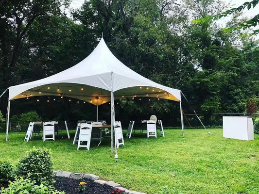 20x20 high peak tent set up on grass with string lights, tables and white folding chairs